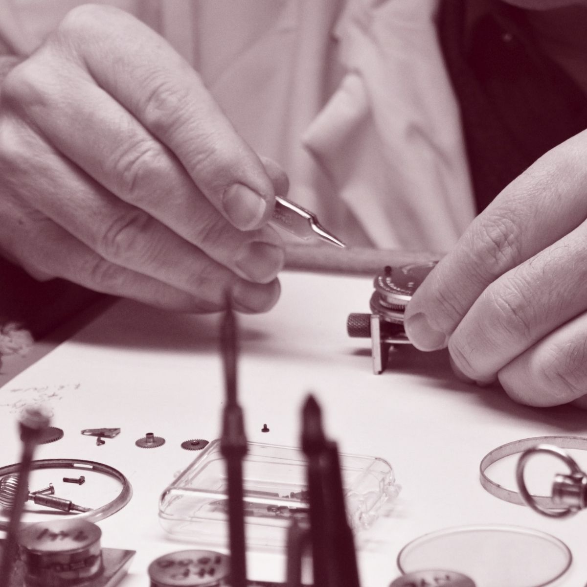 Close-up of hands working on a small mechanical object with tools on a table.